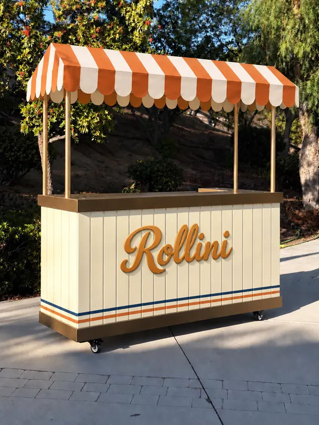 The Rollini event cart with a scalloped orange and cream awning, gold posts and navy and orange pinstripes