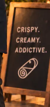A Rollini sidewalk chalkboard reading Crispy. Creamy. Addictive.